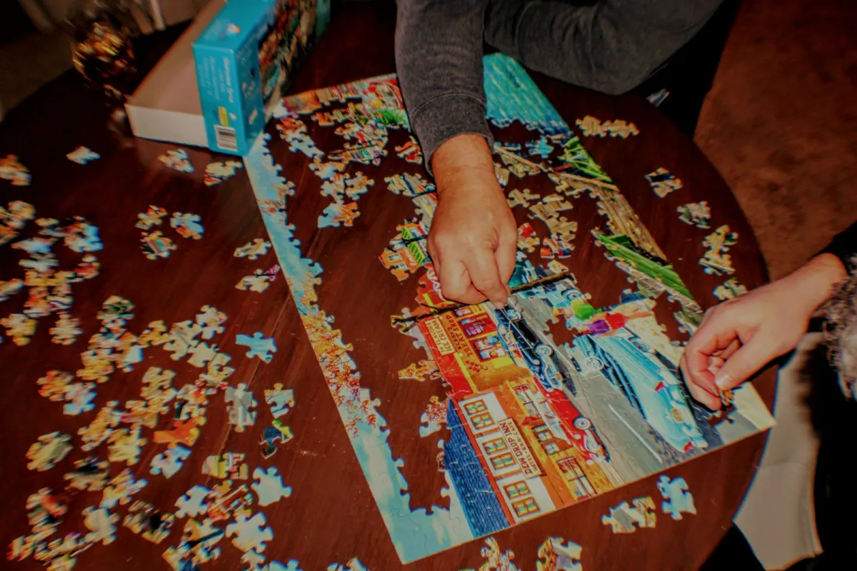 Hands piecing together a jigsaw puzzle on a wooden table