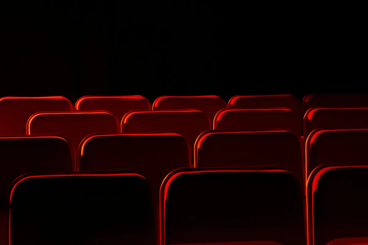 Rows of empty red theatre seats lit from the side in a dark auditorium