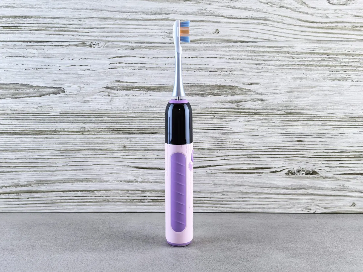 A purple electric toothbrush standing upright against a pale wooden background A purple electric toothbrush standing upright against a pale wooden background