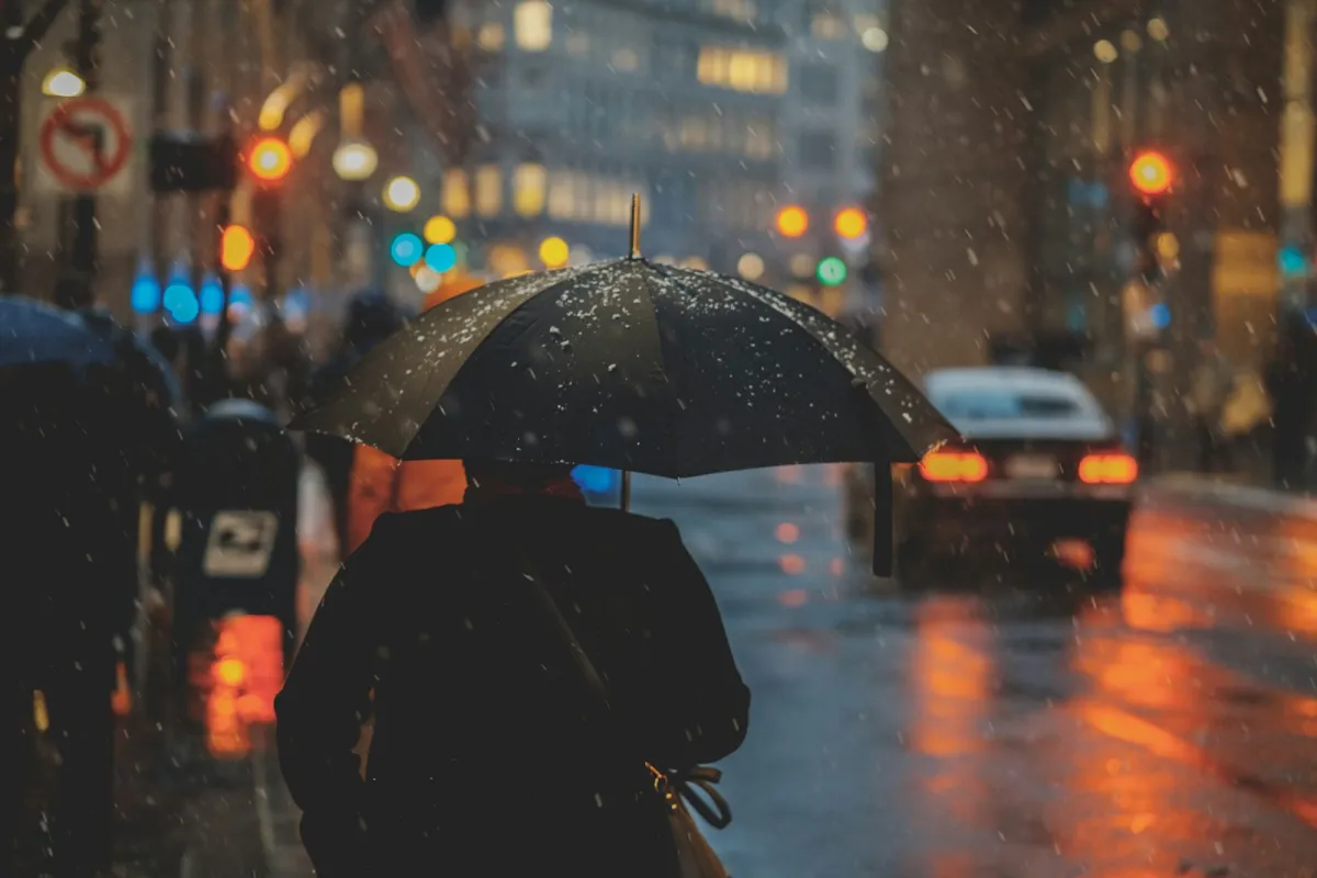 A person walking down a city street under a black umbrella in falling snow and rain A person walking down a city street under a black umbrella in falling snow and rain