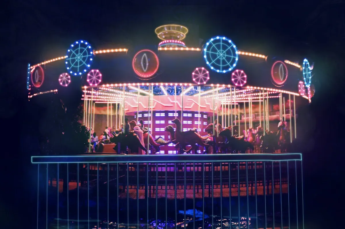 A carousel lit up with blue, pink and orange lights inside a dark indoor theme park