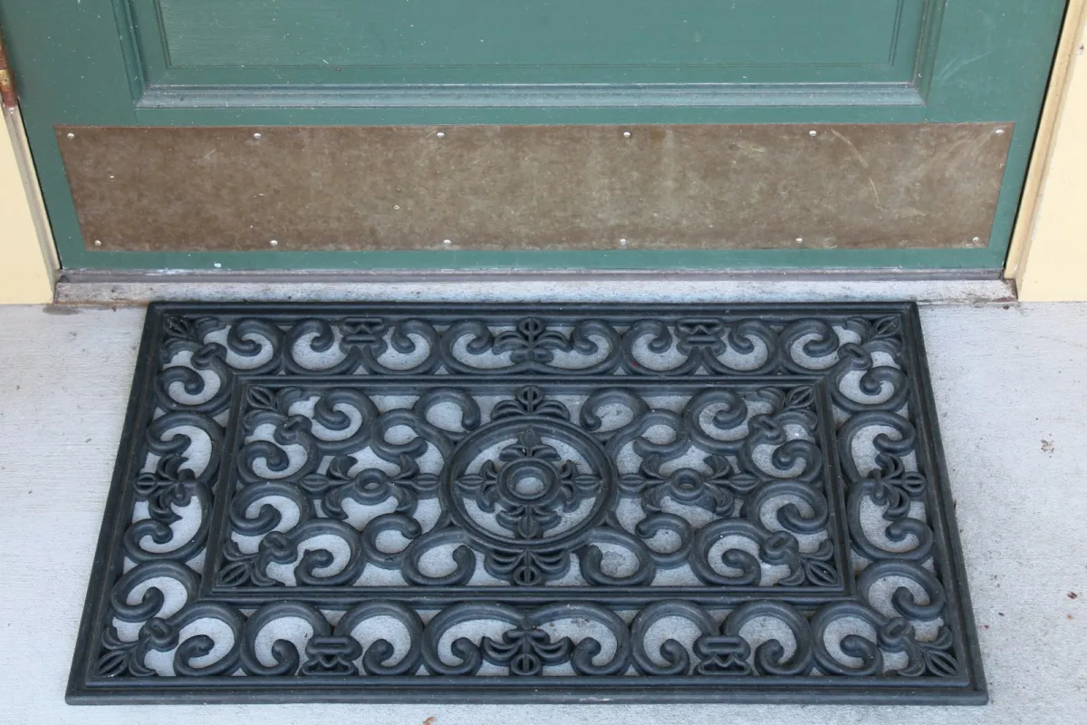 A black scrollwork rubber door mat in front of a green front door