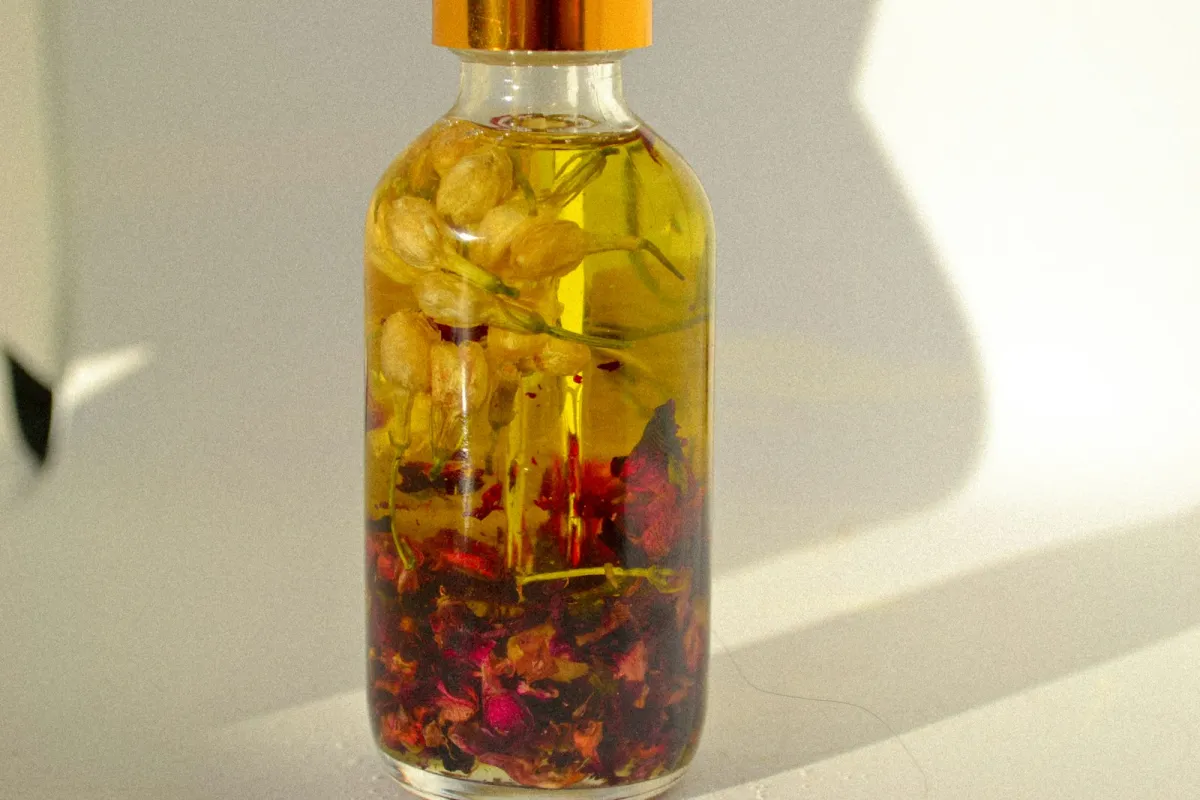 Glass bottle of golden oil surrounded by jasmine buds and red rose petals Glass bottle of golden oil surrounded by jasmine buds and red rose petals