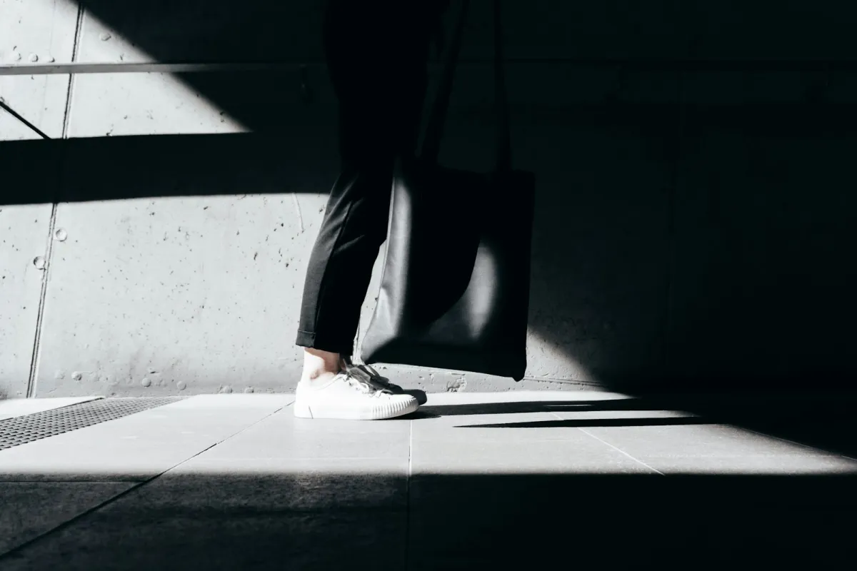 Someone in plain white trainers and black trousers standing in a sunlit concrete corridor Someone in plain white trainers and black trousers standing in a sunlit concrete corridor