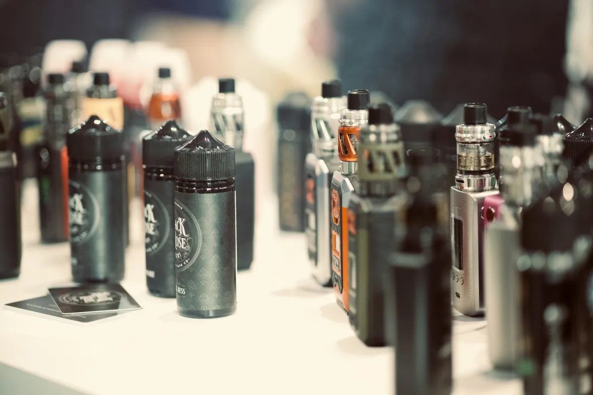 Rows of e-liquid bottles and vape kits on a white table Rows of e-liquid bottles and vape kits on a white table