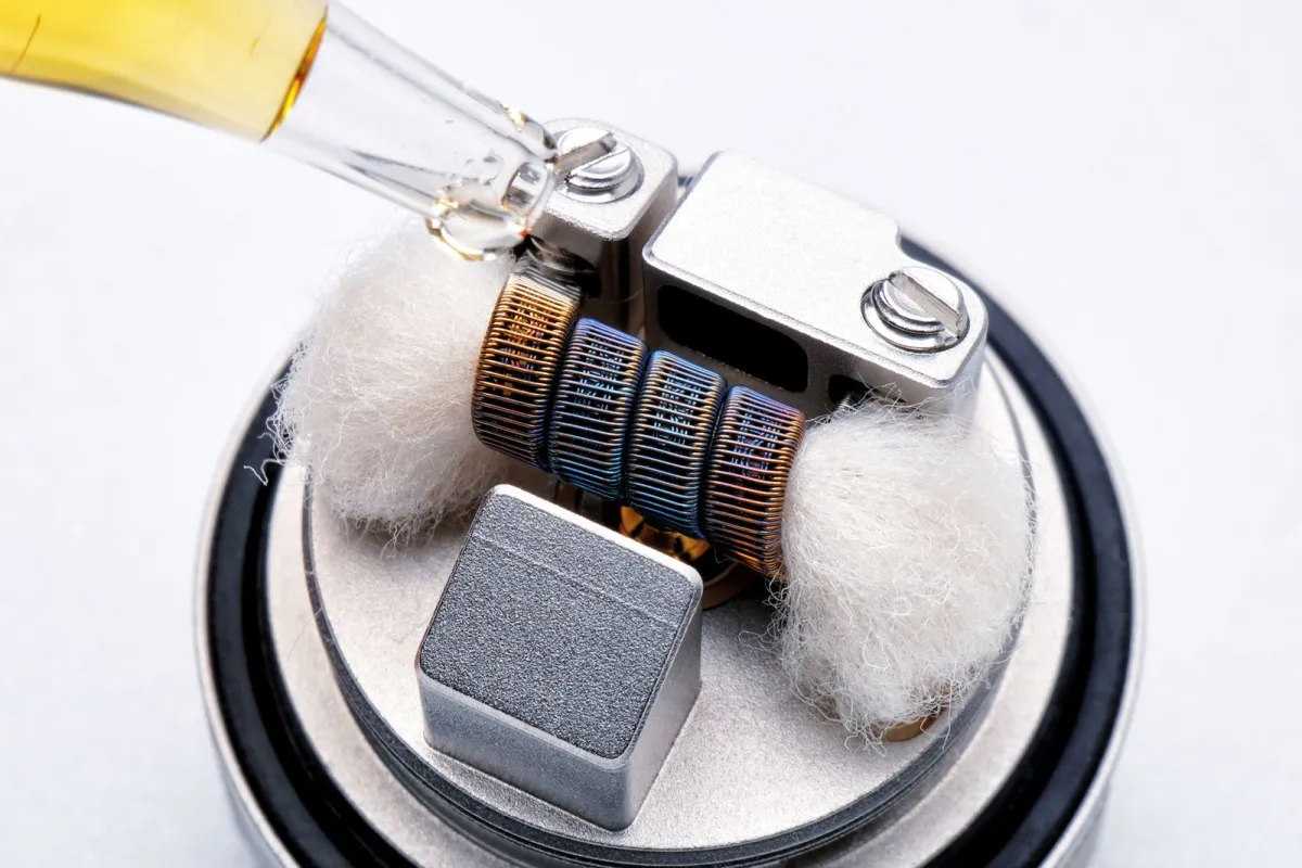 Close-up of a dropper adding e-liquid to the cotton and coil of a vape atomiser Close-up of a dropper adding e-liquid to the cotton and coil of a vape atomiser