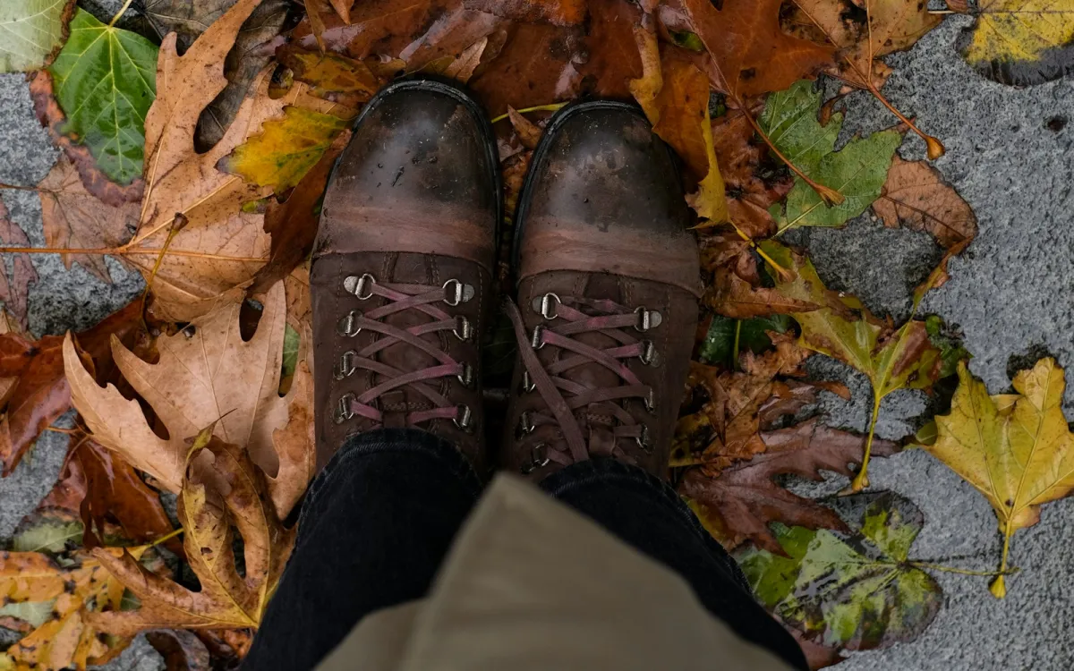 Looking down at a pair of brown lace-up boots standing on wet autumn leaves on a pavement Looking down at a pair of brown lace-up boots standing on wet autumn leaves on a pavement
