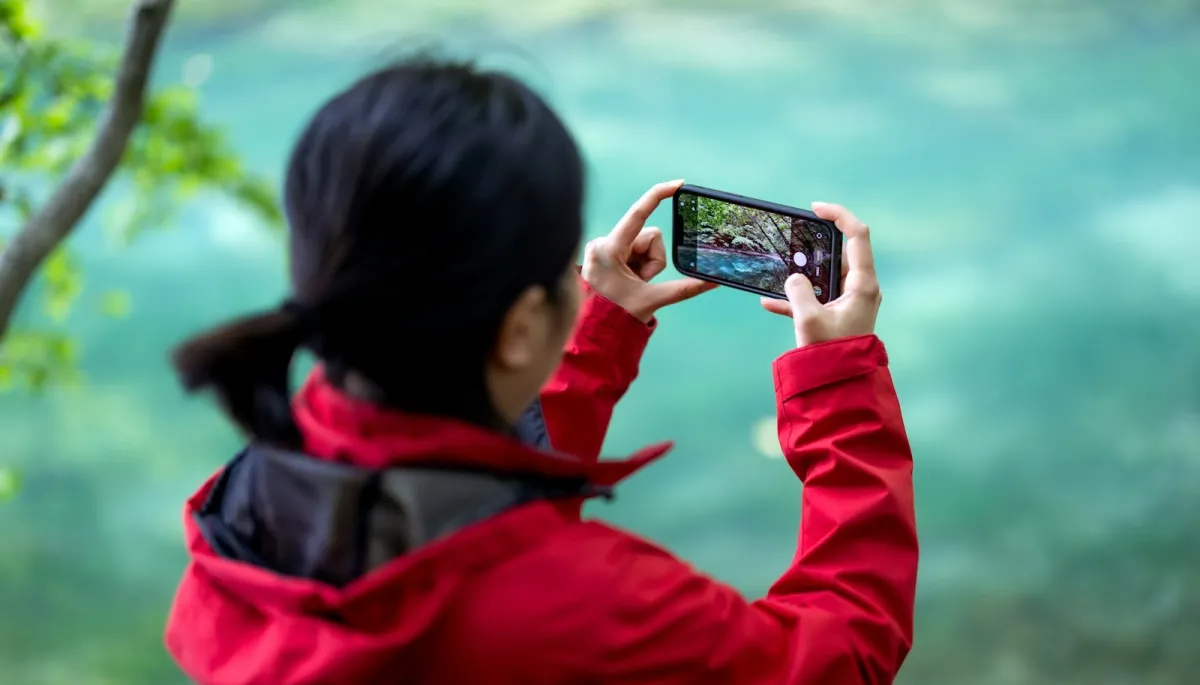Traveller in a red jacket photographing a turquoise river with a smartphone