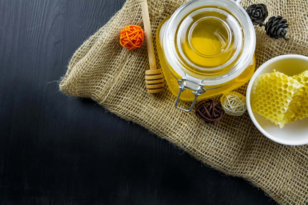 A glass jar of honey with a wooden dipper and a bowl of honeycomb on hessian cloth A glass jar of honey with a wooden dipper and a bowl of honeycomb on hessian cloth