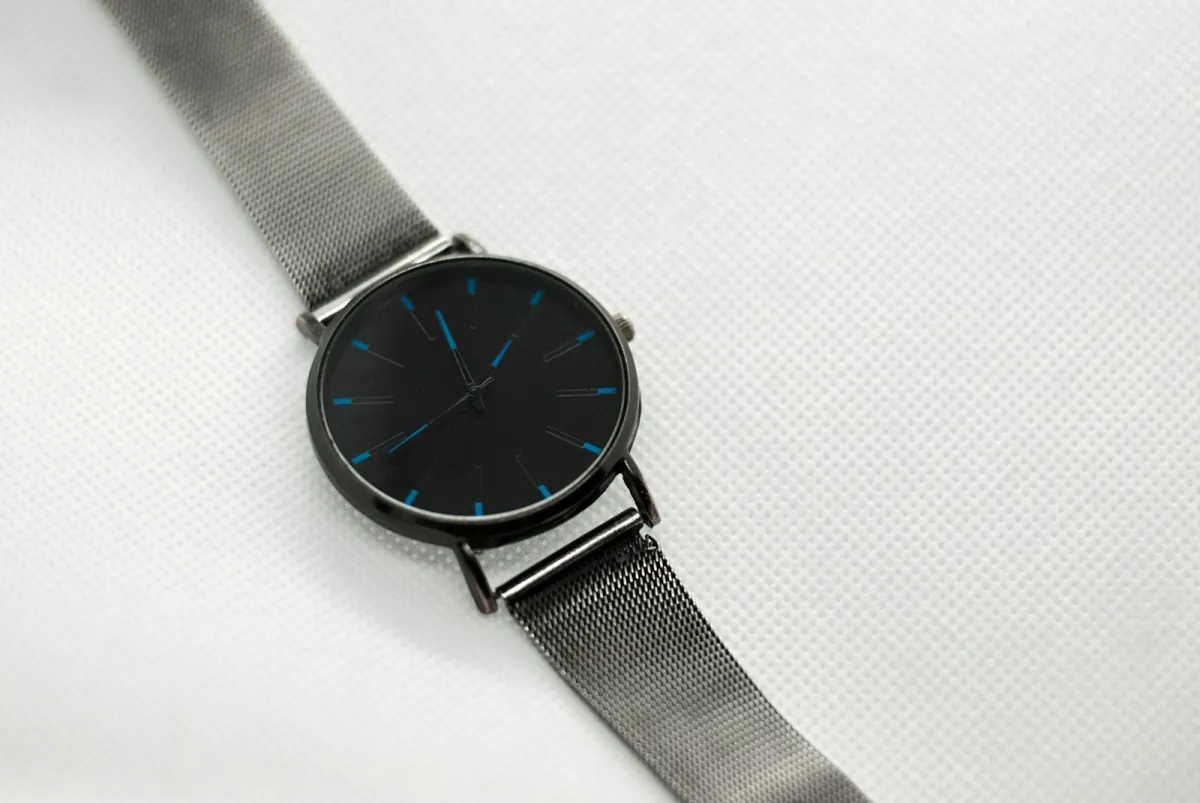 Minimal black-dial wristwatch with a grey mesh strap lying on white fabric