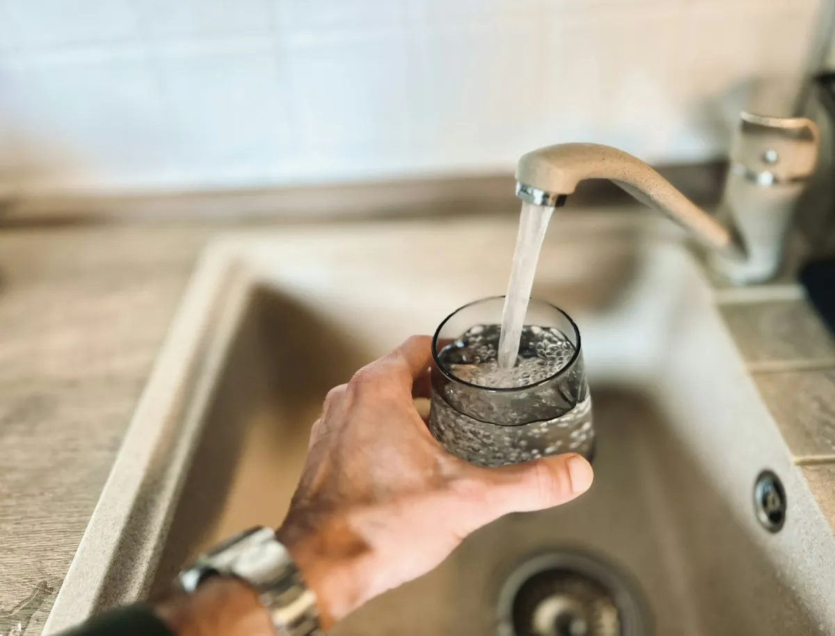 A hand filling a glass with water from a kitchen tap A hand filling a glass with water from a kitchen tap