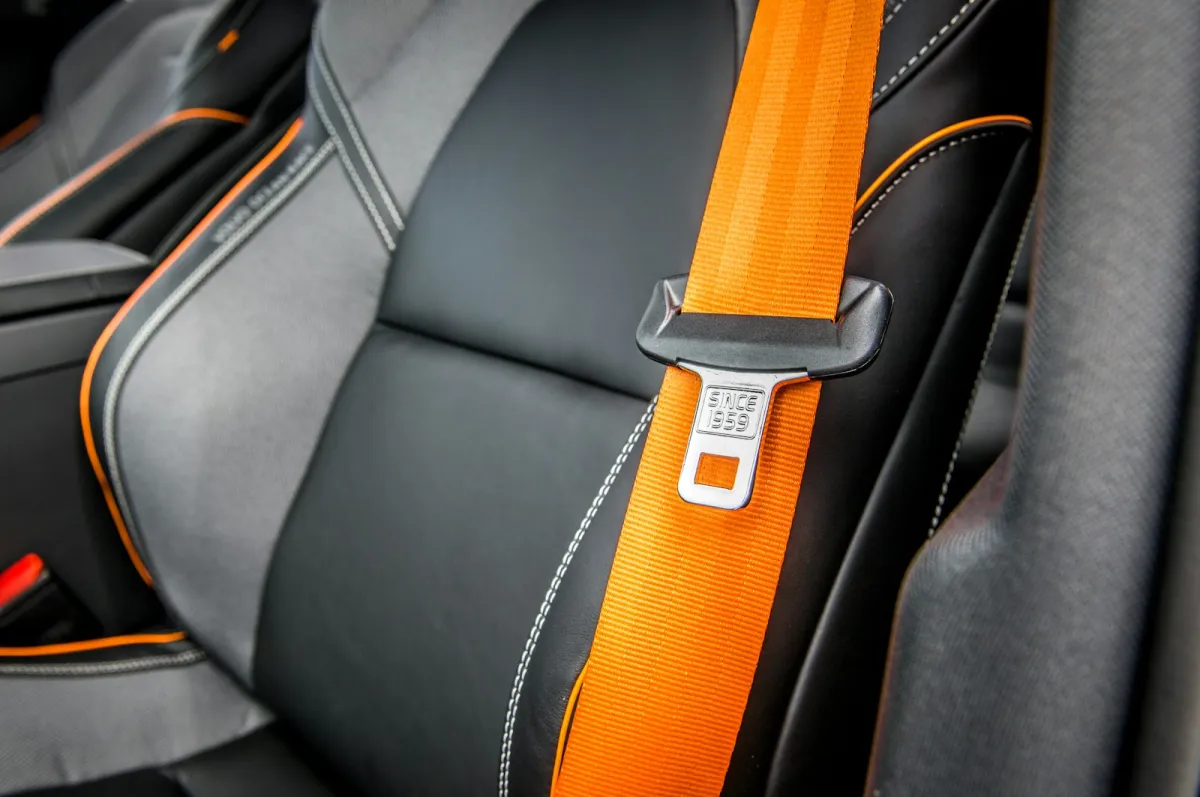 An orange seat belt and buckle across a black leather car seat