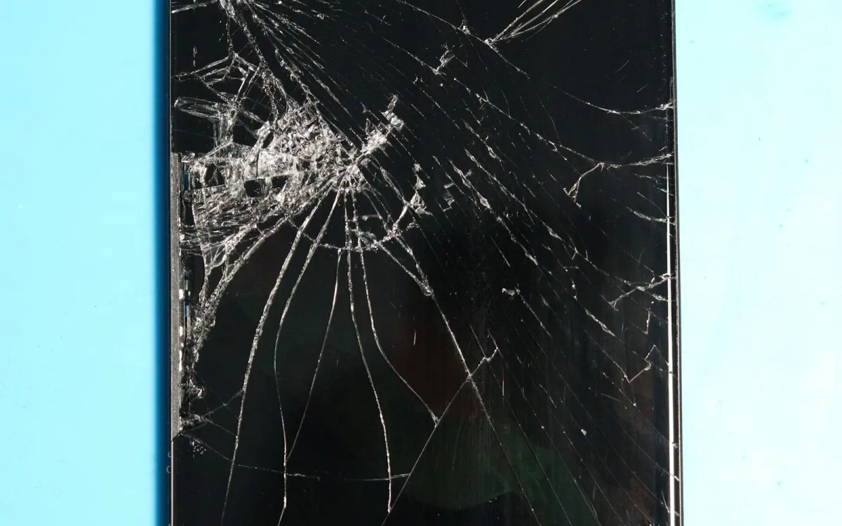 A smartphone with a badly cracked screen on a light blue surface