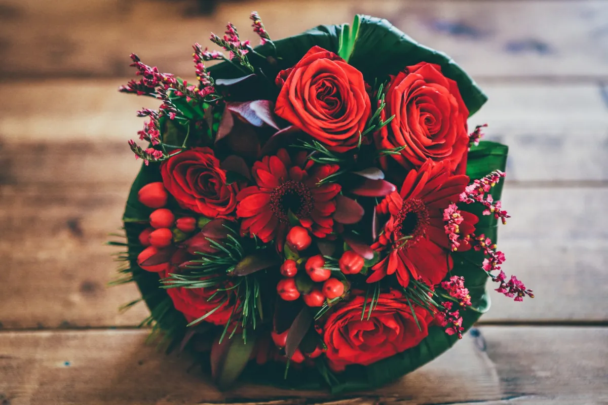 A bouquet of red roses, gerberas and berries on a wooden table