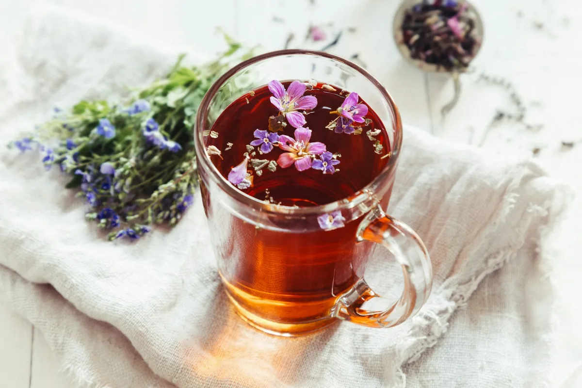 A glass mug of herbal tea with floating flowers beside a bunch of wild blooms