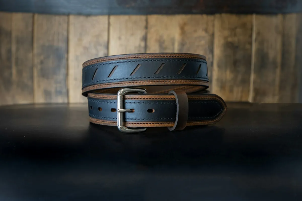 A coiled black and tan leather belt on a dark table in front of weathered wooden boards