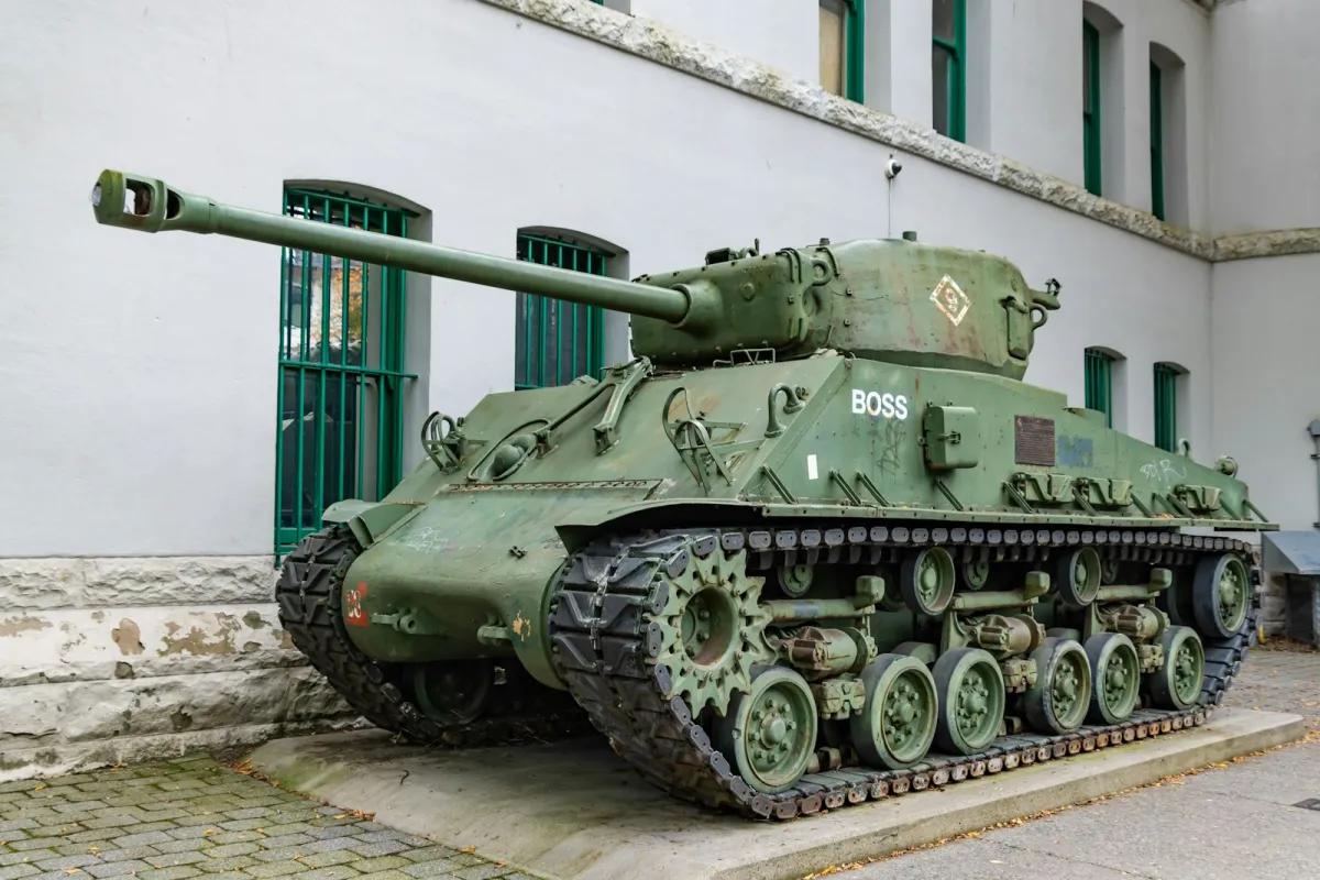 A green Sherman tank on display outside a white stone building A green Sherman tank on display outside a white stone building