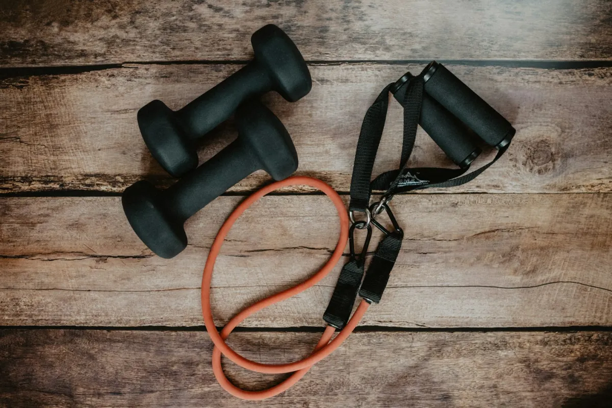 Two black dumbbells and an orange resistance band on a wooden floor Two black dumbbells and an orange resistance band on a wooden floor