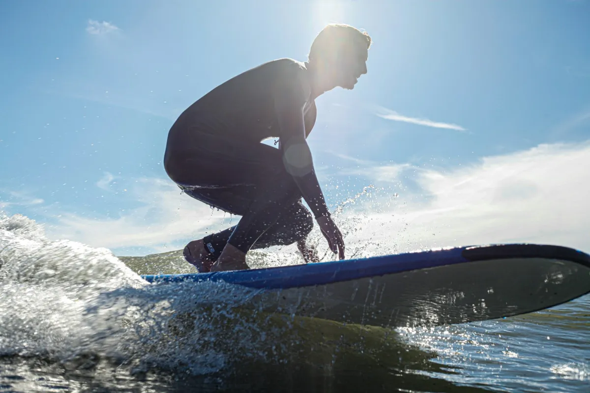 A surfer in a full wetsuit, silhouetted against the sun, crouching low on a longboard A surfer in a full wetsuit, silhouetted against the sun, crouching low on a longboard