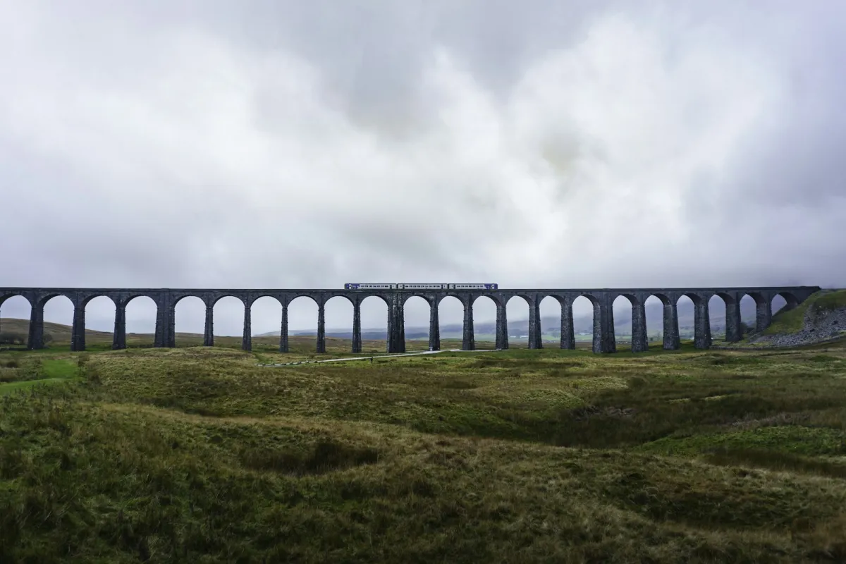 A train crossing a stone viaduct in the Yorkshire Dales on a cloudy day