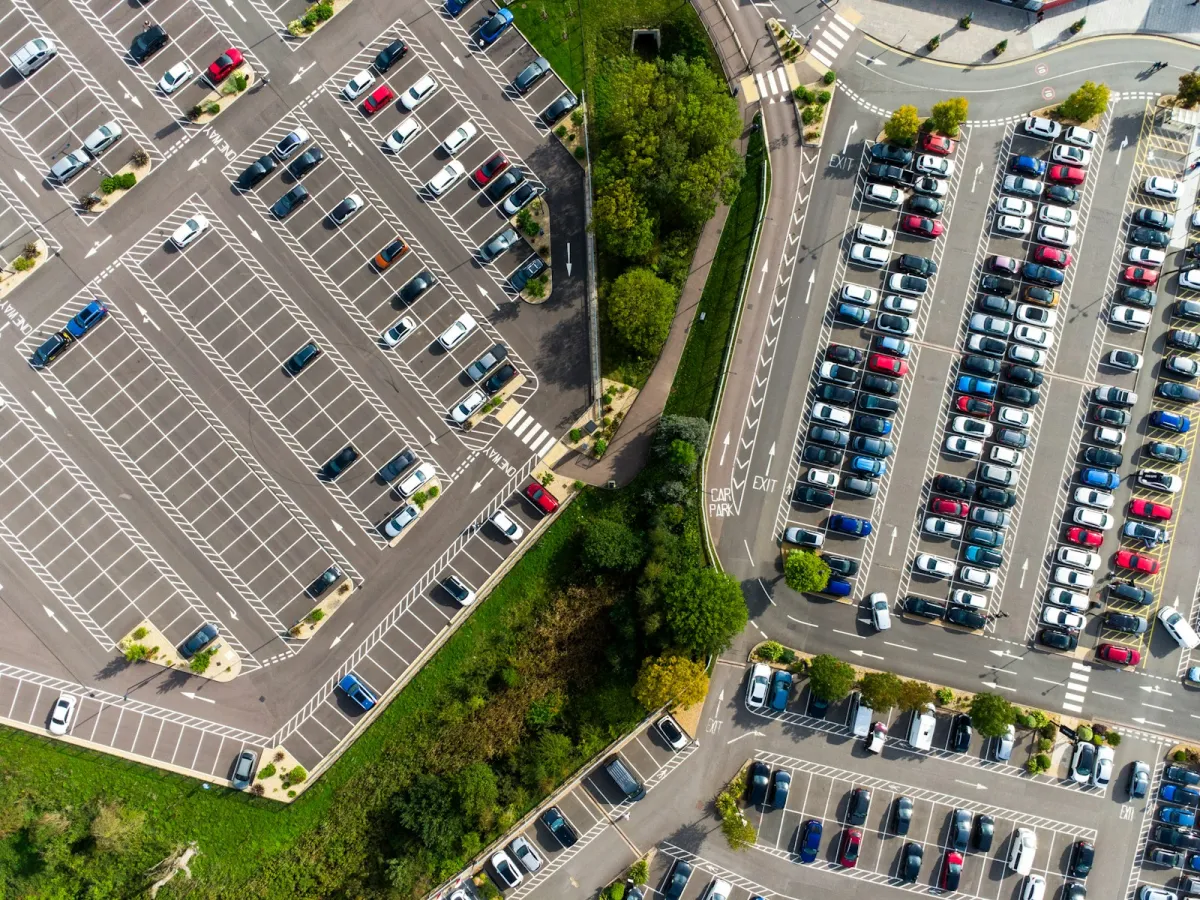 Aerial view of a large car park with rows of parked cars and trees