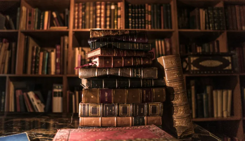 A stack of old leather-bound books in front of shelves full of books