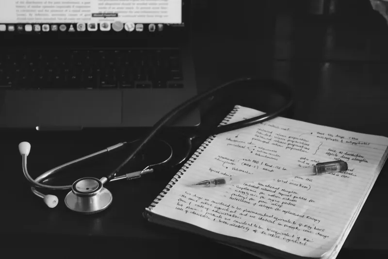 A stethoscope and handwritten notes beside a laptop