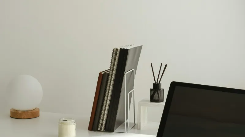 Minimal white desk with a laptop, notebooks in a rack, a globe lamp and a candle