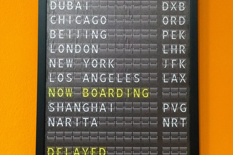 A split-flap departures board listing world cities with a delayed flight