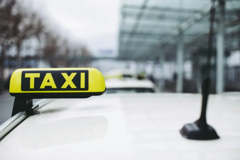 Yellow taxi sign on the roof of a white car outside an airport terminal