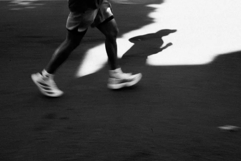 Black and white photo of a runner's legs and trainers in motion, casting a long shadow on the road