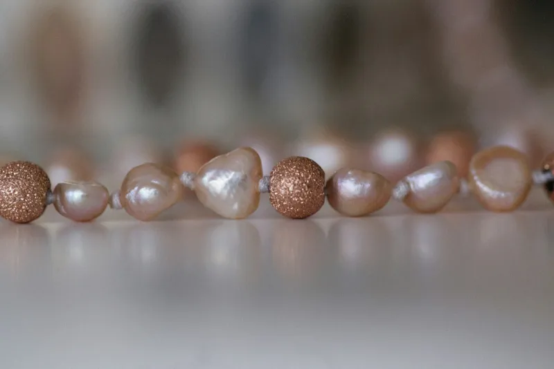 Close-up of a strand of pink baroque pearls and textured gold beads on a white surface