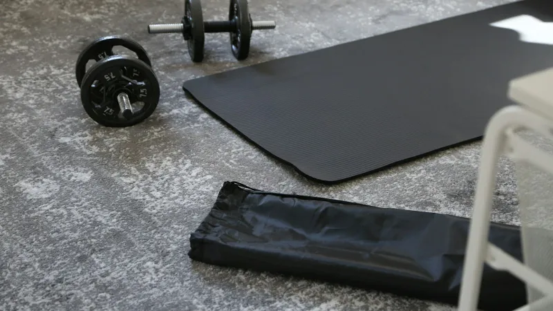 Pair of dumbbells next to a black exercise mat on a grey carpet