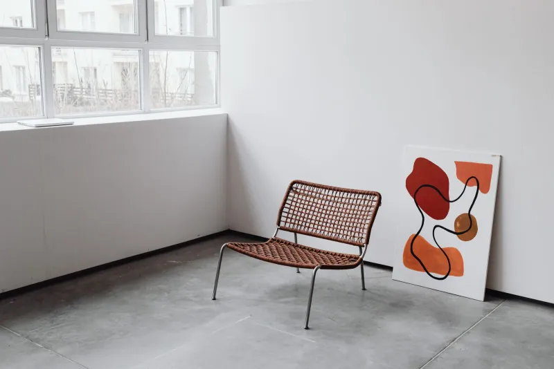 Archer and Ash: Mediterranean canvas prints and gallery wall sets A woven lounge chair beside an abstract orange painting leaning against a white wall
