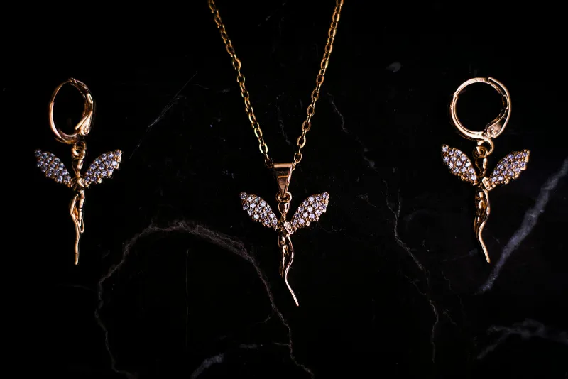A gold pendant necklace and matching drop earrings on dark marble