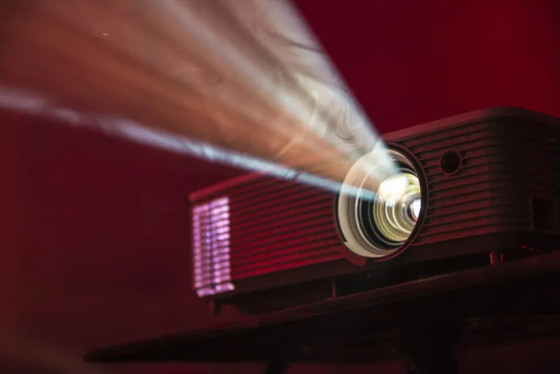 Aurzen: smart and fold-up projectors with free UK delivery A projector on a table casting a beam of light through a dark red room