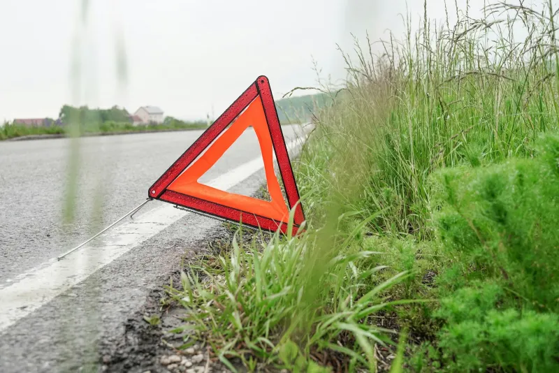 A red warning triangle on the edge of a wet country road