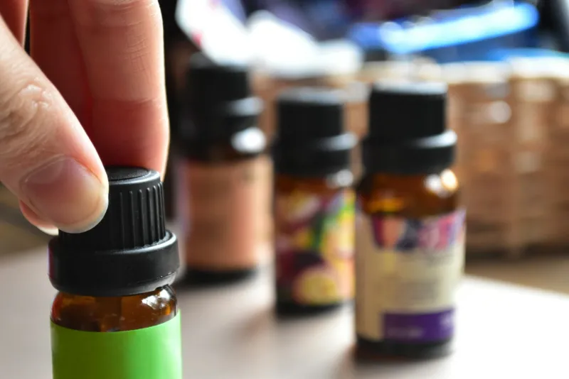 B Calm: organic essential oils, diffusers and gua sha from Essex Fingers lifting a small amber essential oil bottle with more bottles blurred behind