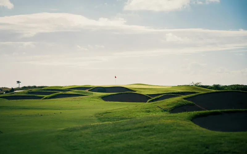 Rolling green golf course with sand bunkers and a red flag on the distant green