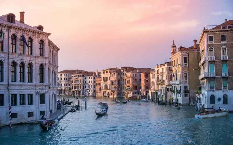 Gondolas moored on Venice's Grand Canal under an orange sunset sky