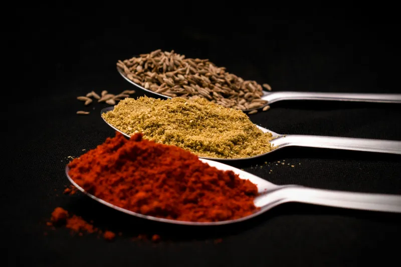 Three spoons of chilli powder, ground coriander and cumin seeds on a dark background