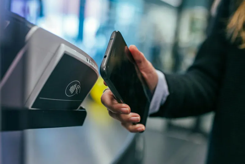 A hand holding a smartphone up to a contactless card reader