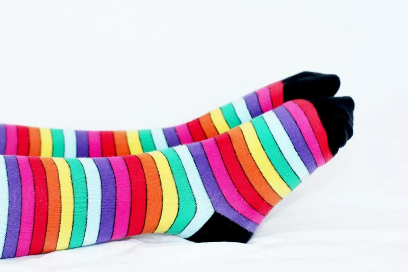 Feet in brightly striped rainbow socks resting on a white background