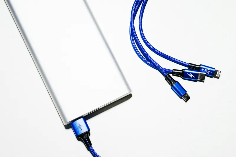 A silver power bank with a blue braided charging cable and a three-way USB cable on a white surface