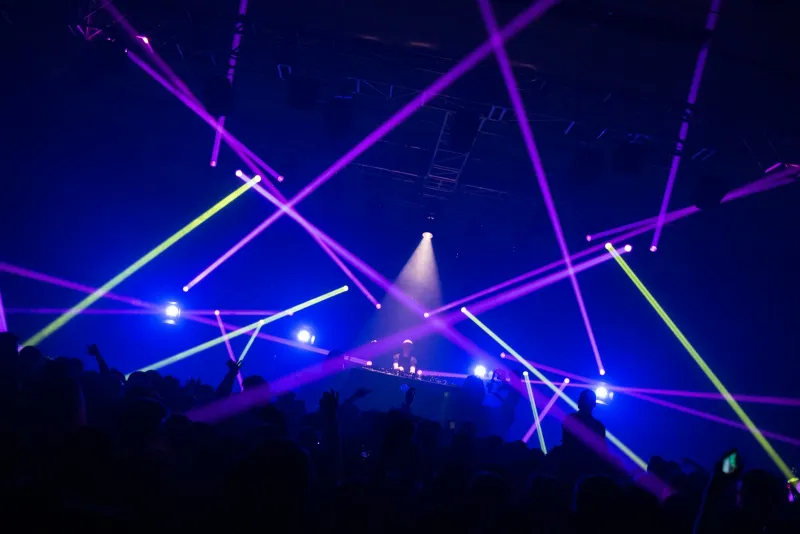 Purple and green laser beams over a silhouetted crowd during a DJ set