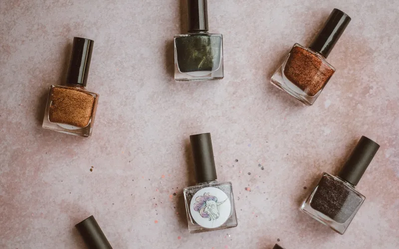 Bottles of glittery brown, green and grey nail polish on a pink surface