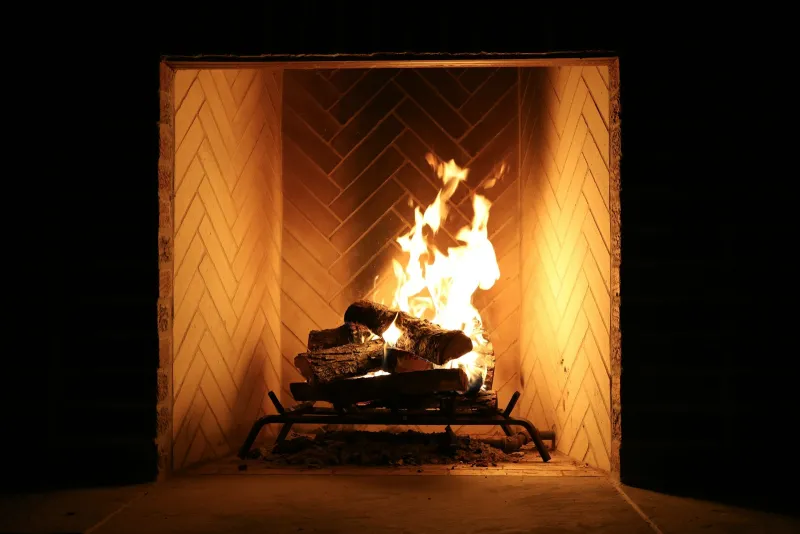 Flames rising from logs in a herringbone brick fireplace at night