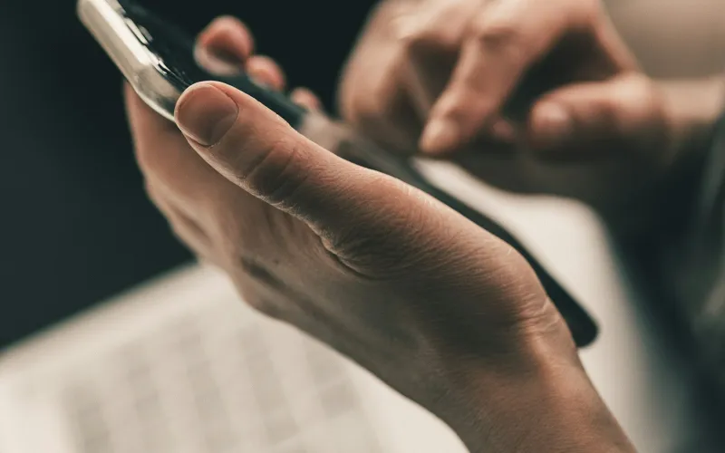 bOnline: VoIP phone systems and business broadband for small firms Hands holding a smartphone above a laptop keyboard