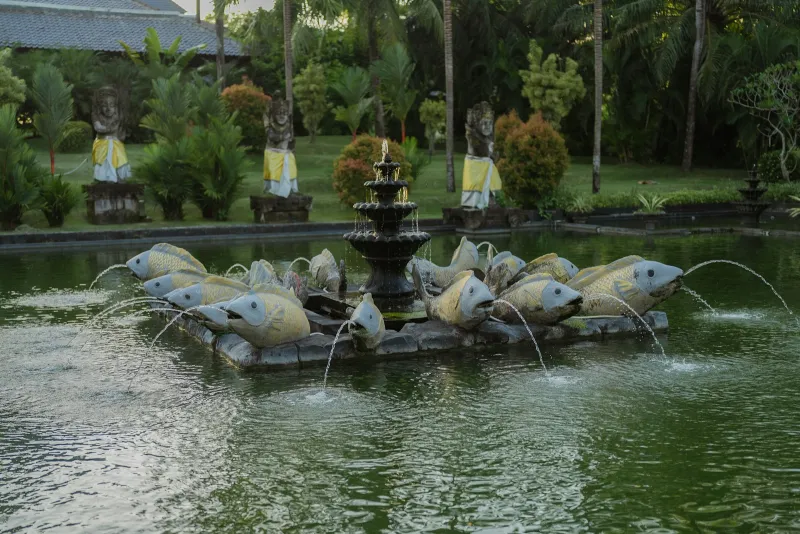 A garden pond with a tiered fountain and fish sculptures spouting water