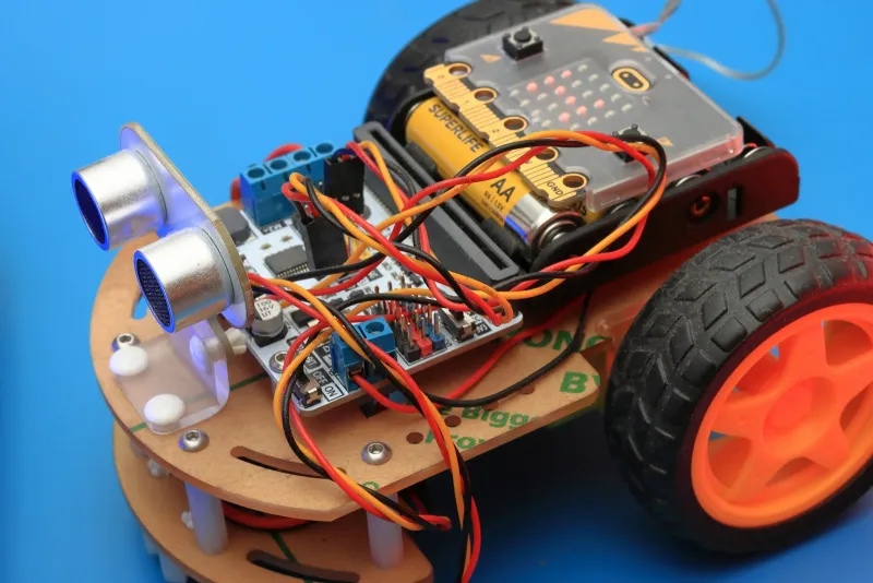 A small wheeled robot kit with a circuit board, sensor and coloured wires